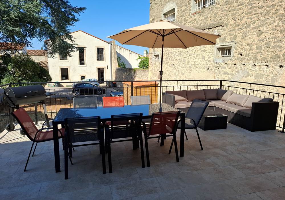 Terrasse du gîte Le Pressoir à Montblanc avec table à manger, barbecue et vue sur le domaine.