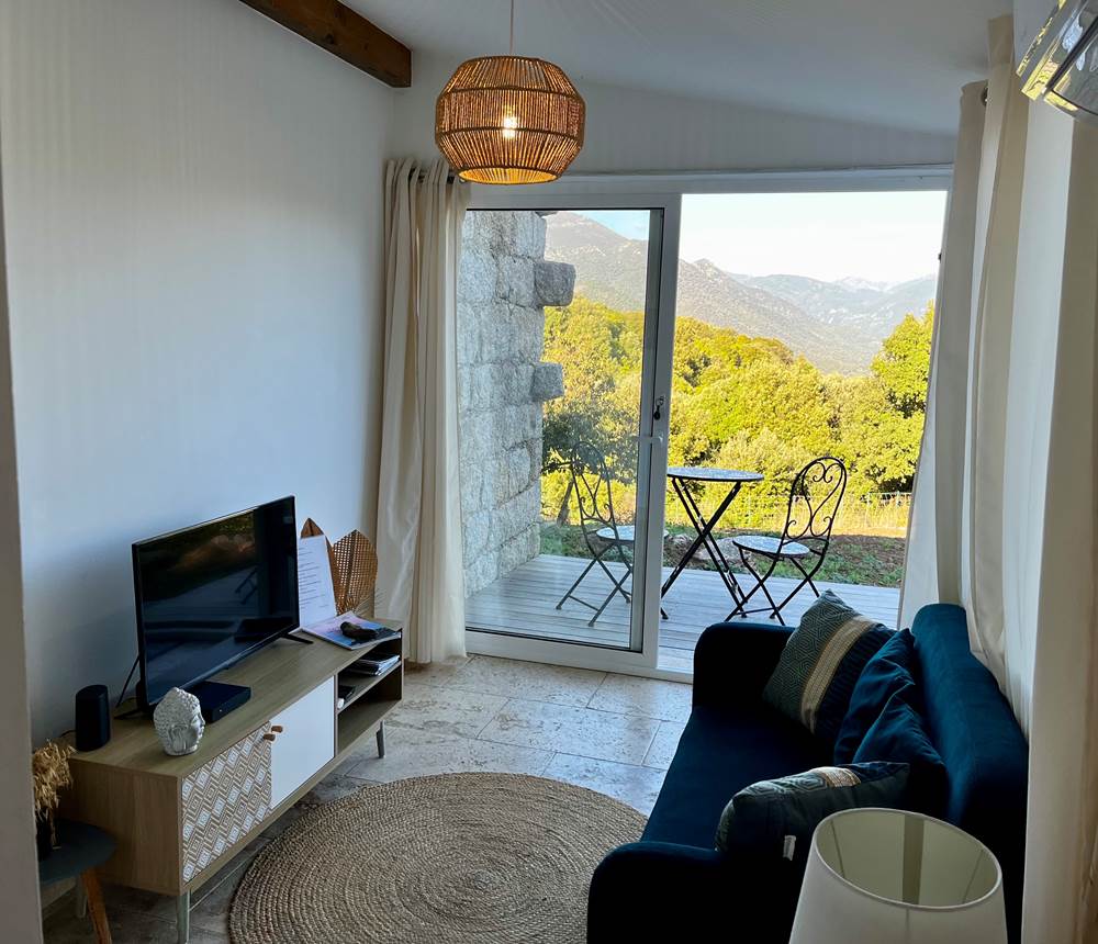 Salon cosy avec vue imprenable sur la nature, baigné de lumière et ouvert sur la terrasse.