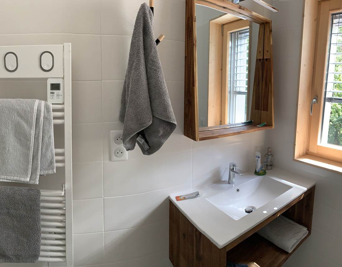 Salle de bain lumineuse avec une douche, une vasque, un grand sèche serviette et des WC.