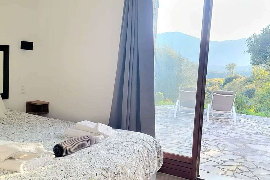 Vue de l'intérieur de la chambre d'amis 4 avec une grande baie vitrée ouvrant sur la nature sauvage et le maquis corse au Domaine Cardu..