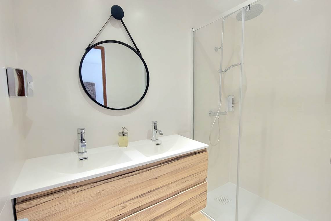 Salle d'eau moderne avec double vasque, douche à l'italienne et miroir rond design.