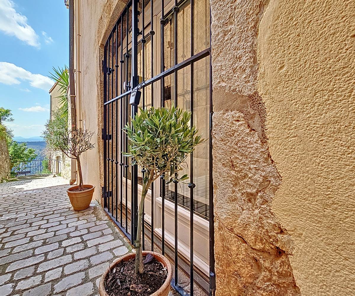 L’entrée se fait par une charmante porte-fenêtre, protégée par une grille en fer forgé typiquement provençale, ouvrant directement sur un petit sentier.