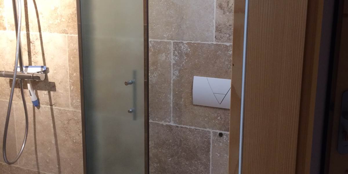 Douche italienne, avec pare douche, on aperçoit le WC suspendu à droite