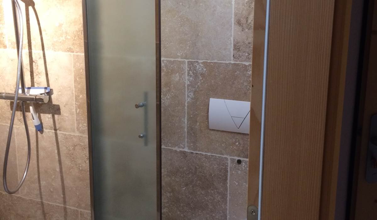 Douche italienne, avec pare douche, on aperçoit le WC suspendu à droite