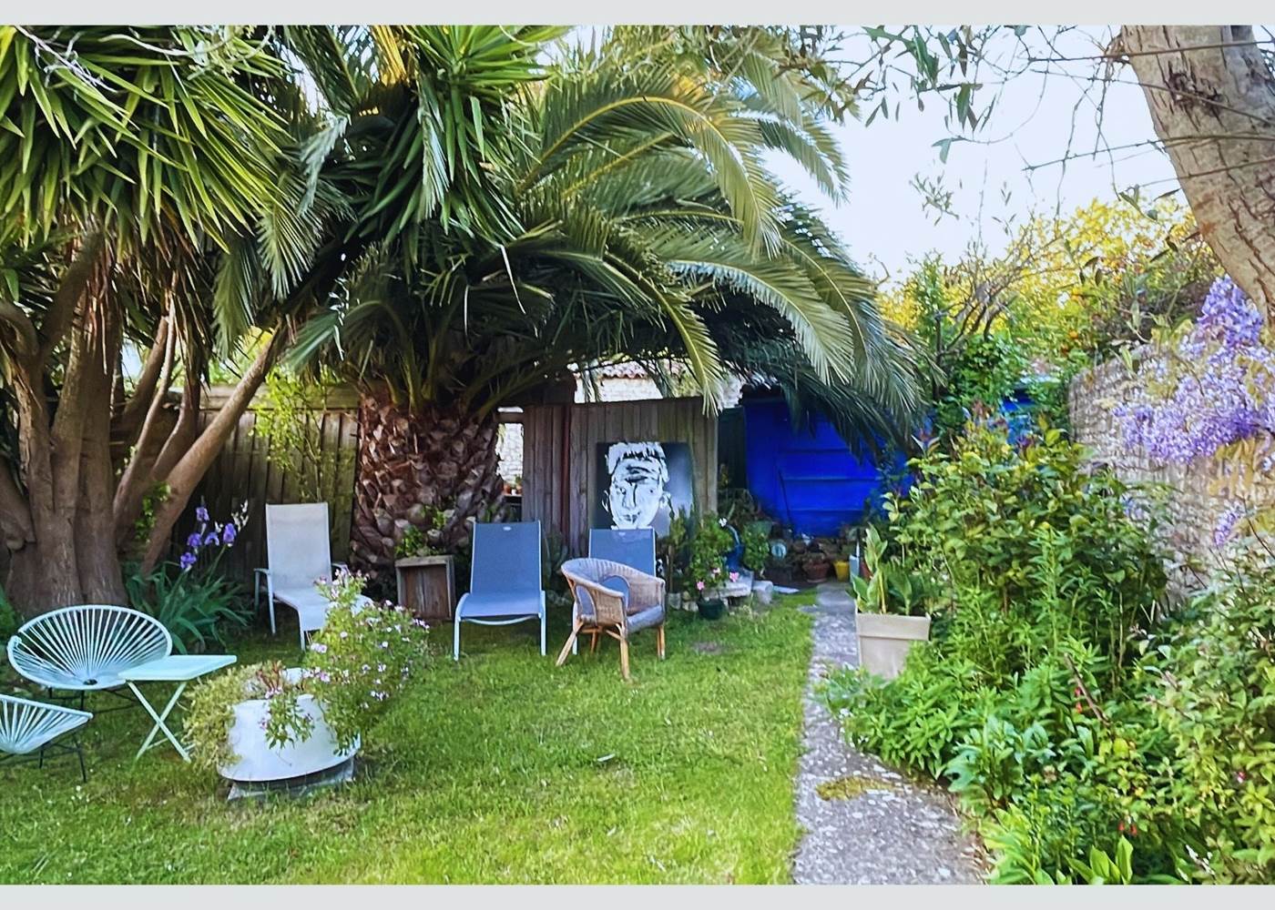 Jardin serein et ombragé : votre pause fraîcheur sous les palmes Entre ombre et lumière, ce coin jardin est un appel au repos. Mobilier confortable, végétation luxuriante et ambiance calme pour un séjour en toute quiétude à La Flotte.