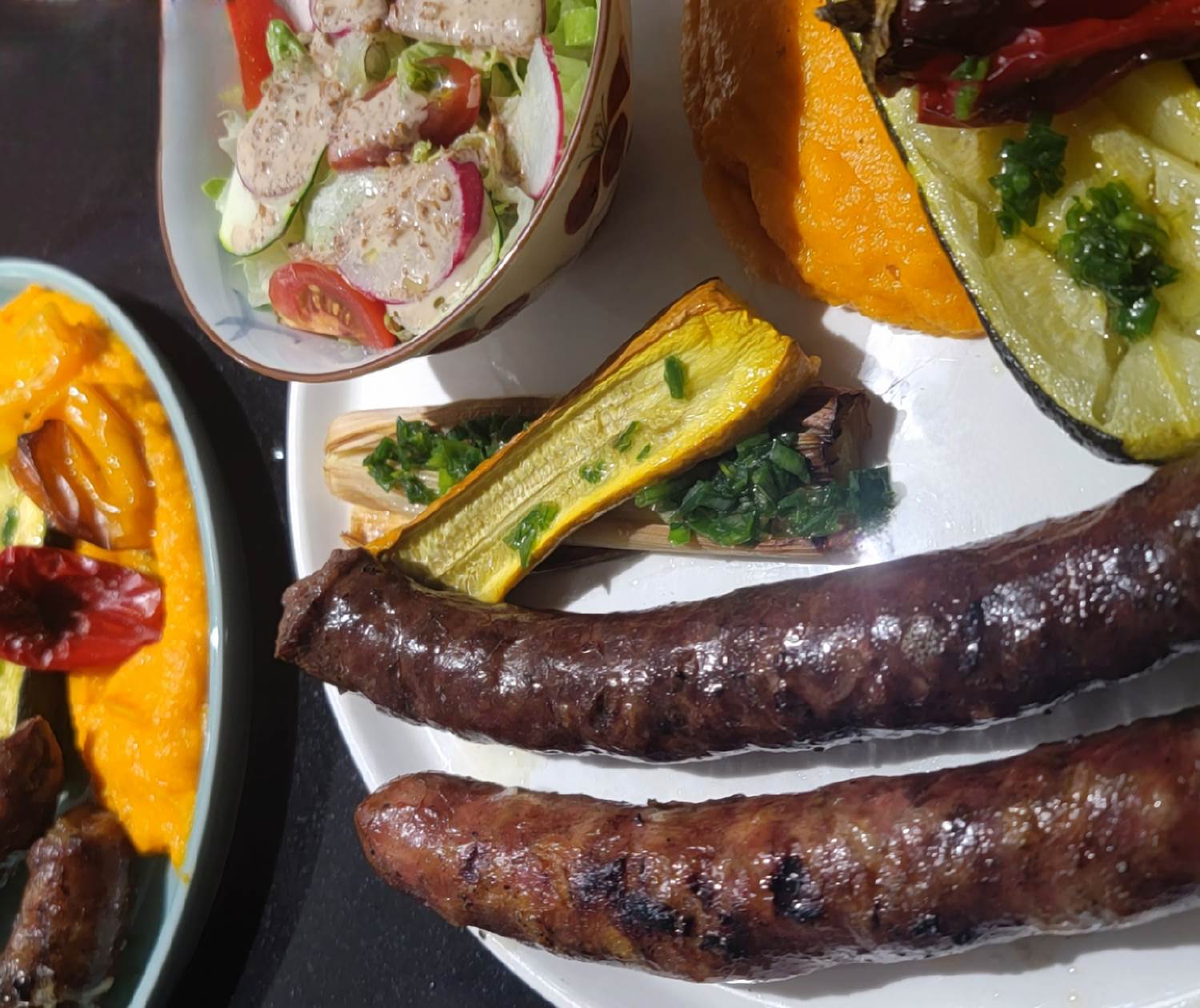 Figatellu et saucisses fumées grillées avec purée de carottes, courgettes confites au four, sauce au poivron et salade asiatique maison.