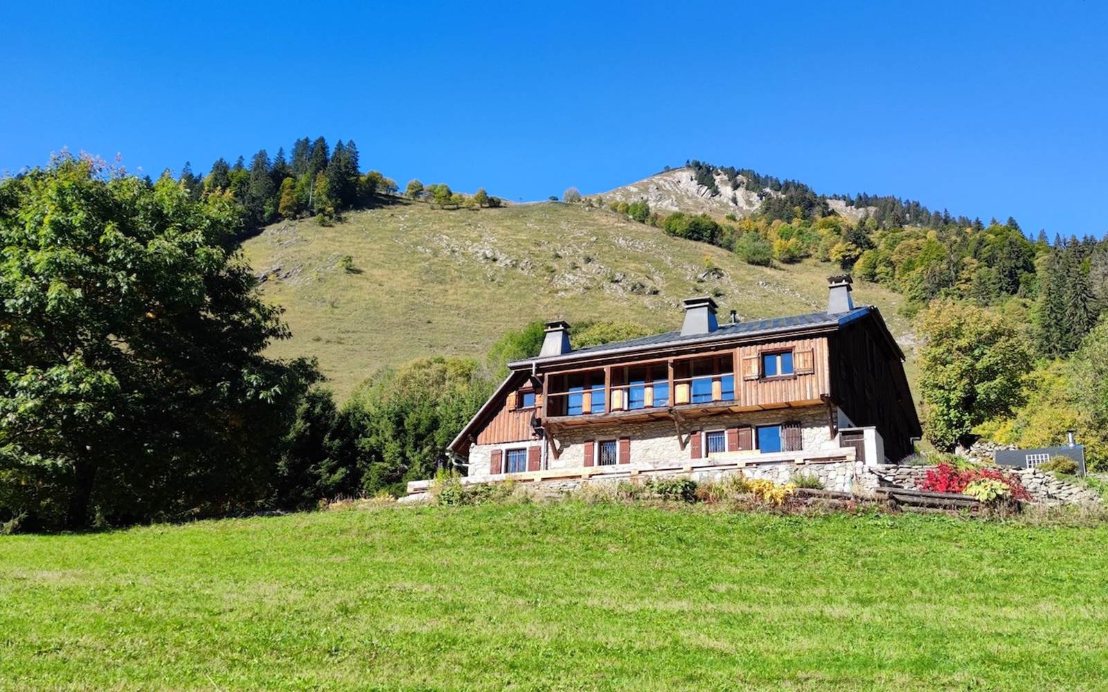 Façade en bois et pierre du chalet de Beauregard au cœur des alpages de Taninges face au massif du Roc d'Enfer