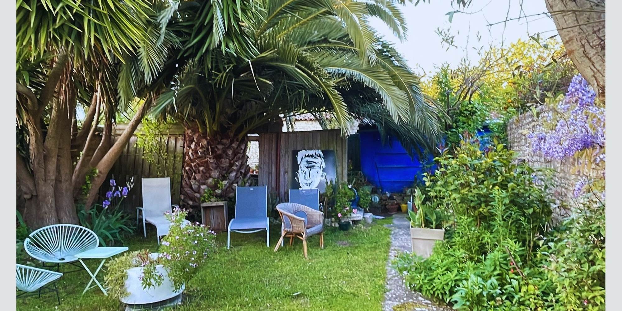 Jardin serein et ombragé : votre pause fraîcheur sous les palmes Entre ombre et lumière, ce coin jardin est un appel au repos. Mobilier confortable, végétation luxuriante et ambiance calme pour un séjour en toute quiétude à La Flotte.
