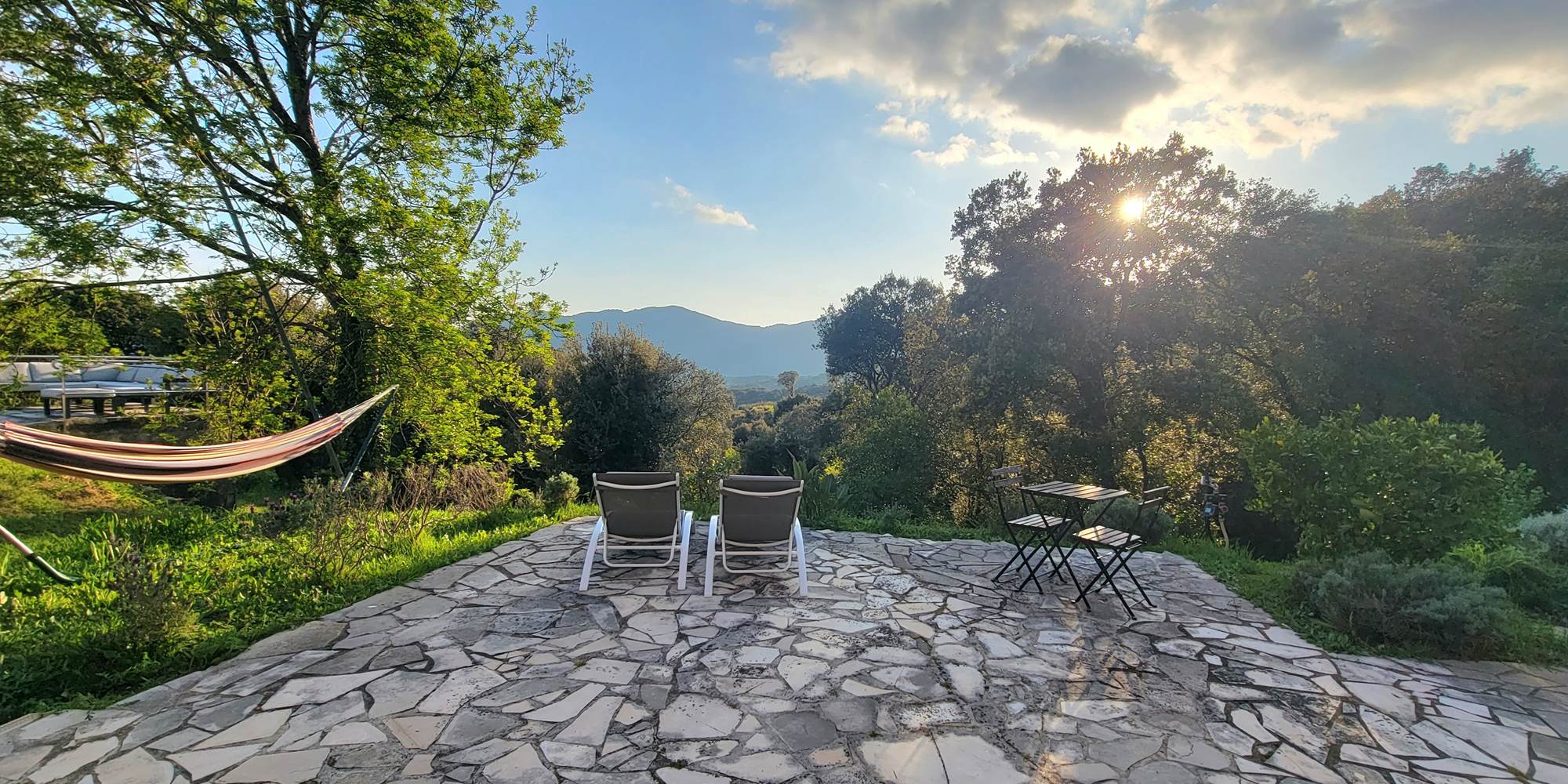 Terrasse en pierre avec chaises longues offrant une vue imprenable sur le coucher de soleil corse.