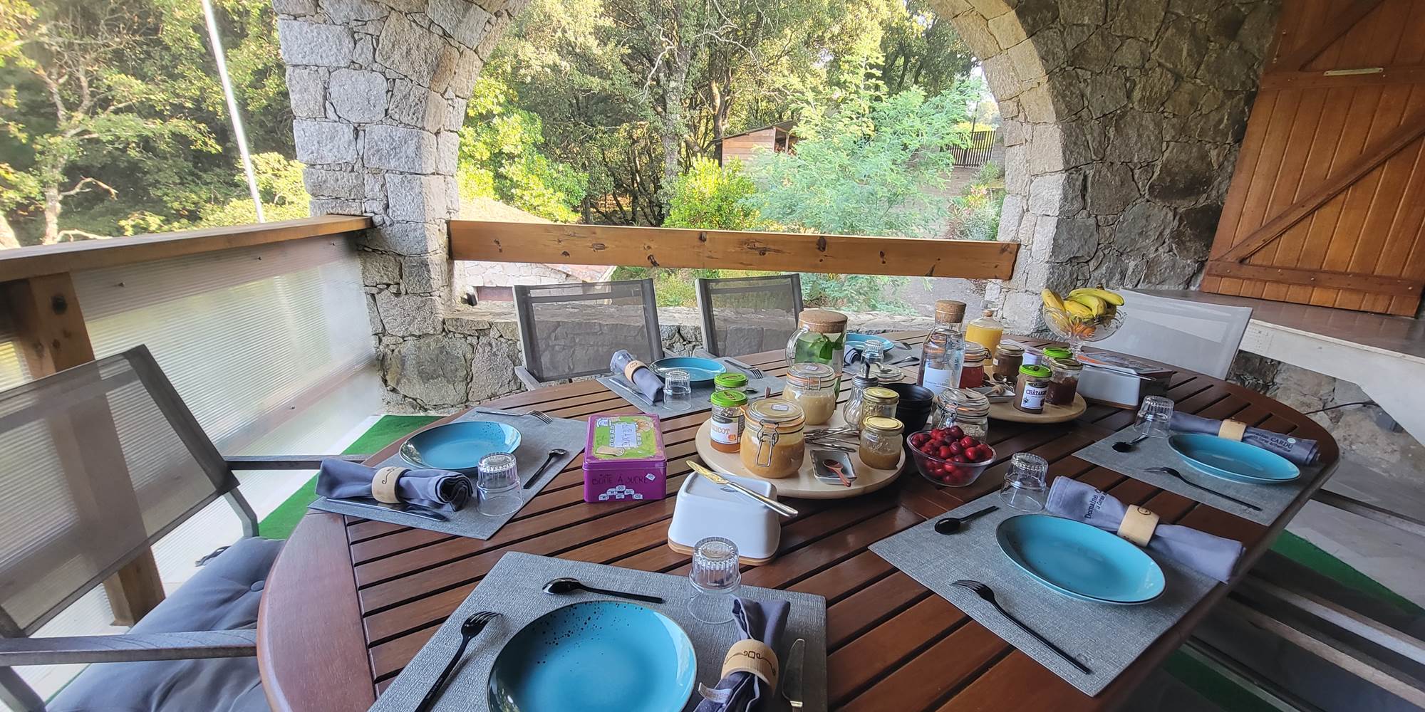 Table d'hôtes de charme dressée sur la terrasse en pierre pour un petit-déjeuner convivial en Corse.