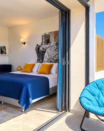 Vue sur la chambre principale de la Junior Suite depuis la terrasse, avec lit double, espace bureau, décoration artistique et accès direct à l'extérieur.