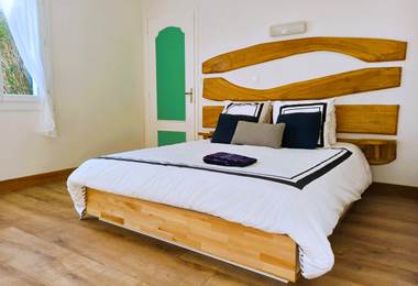 Chambre double lit queen size avec tête de lit bois sculpté, parquet chaud et literie blanche – chambre de charme Lauzerte Quercy Blanc
