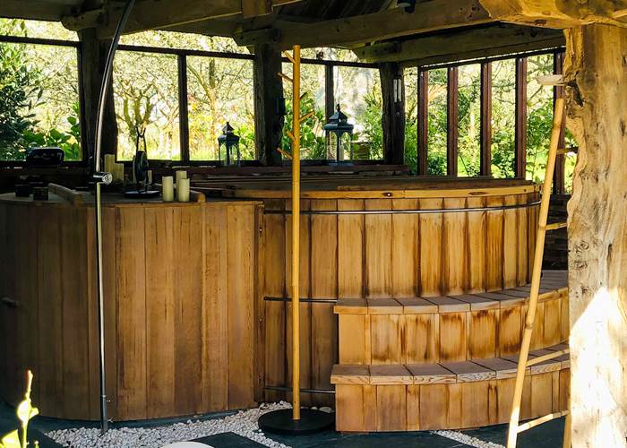 un grand bain en cèdre rouge abrité sous un joli préau
