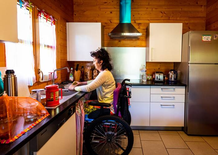 Personne en fauteuil roulant devant le plan de travail d'une cuisine adaptée dans l'un des chalets Bon Air