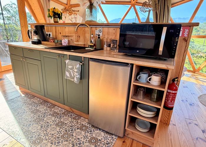 Coin cuisine équipé avec évier, frigo, micro-ondes, cafetière, bouilloire, et vaisselles