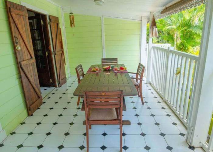 Varangue couverte avec table à manger en bois donnant sur un jardin tropical.