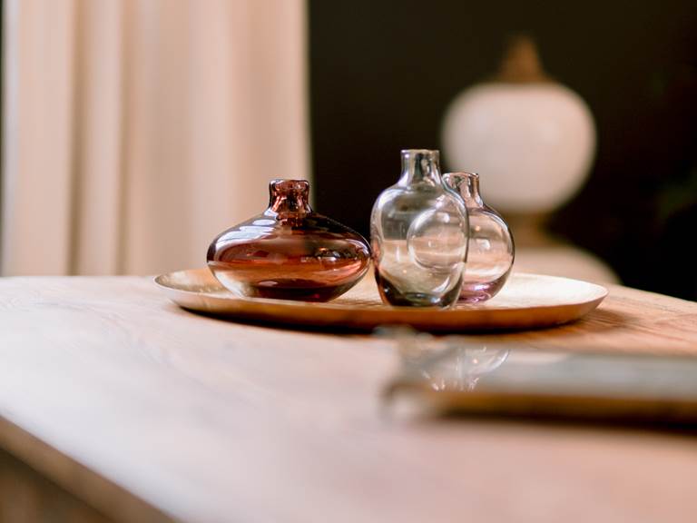 De´tail de vases colore´s en verre transparent, apportant une touche zen, pose´ sur un plateau dore´, lui-me^me sur une table en bois. Equillibre harmonieux et esthe´tique apaisante.