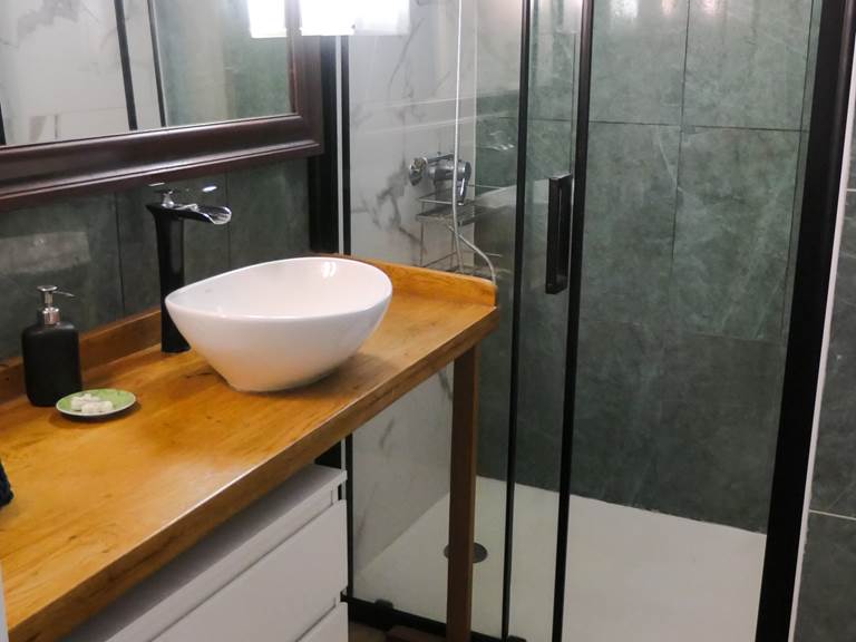 Salle de bain moderne avec vasque à poser sur plan en bois, douche italienne carrelage vert et miroir encadré