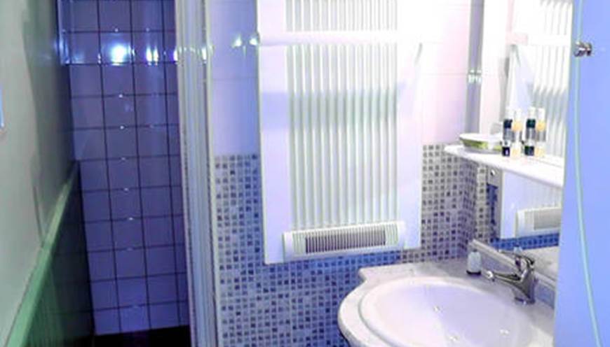 Salle d'eau avec cabine de douches, vasque, sèche serviettes, sèche cheveux, articles de toilette.