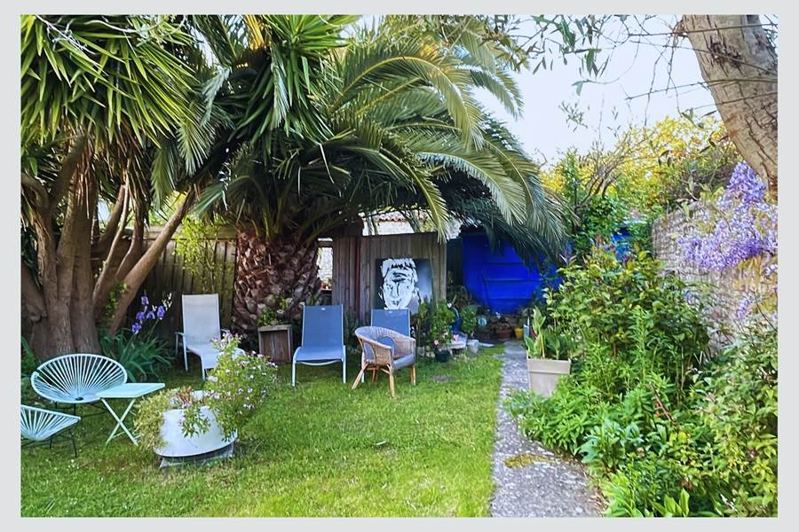 Jardin serein et ombragé : votre pause fraîcheur sous les palmes Entre ombre et lumière, ce coin jardin est un appel au repos. Mobilier confortable, végétation luxuriante et ambiance calme pour un séjour en toute quiétude à La Flotte.